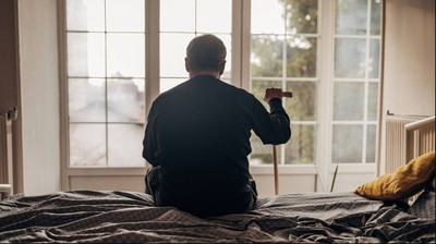 Hombre sentado en la cama con bastón en la mano